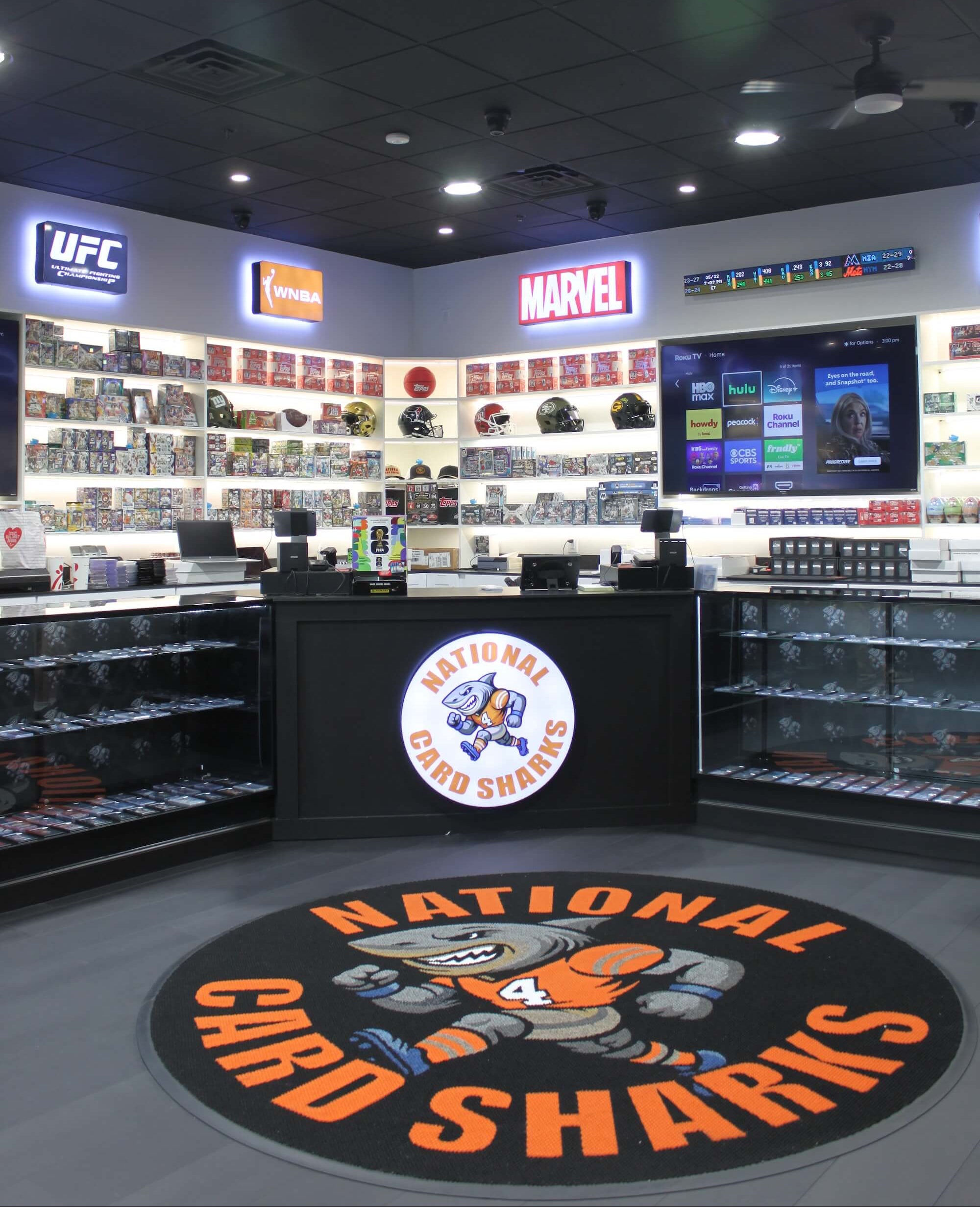 Store interior with shelves displaying collectibles and a 'National Card Sharks' logo on the floor.